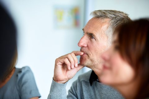 A grey-haired man listens intently during a meeting