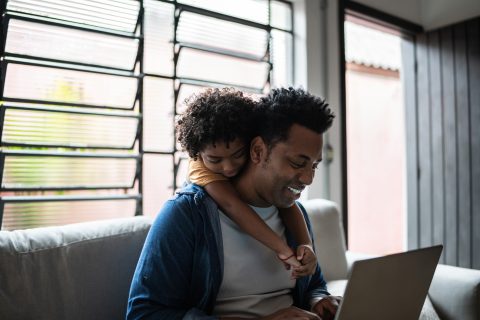 A young child hangs off of his father's back while they shop online