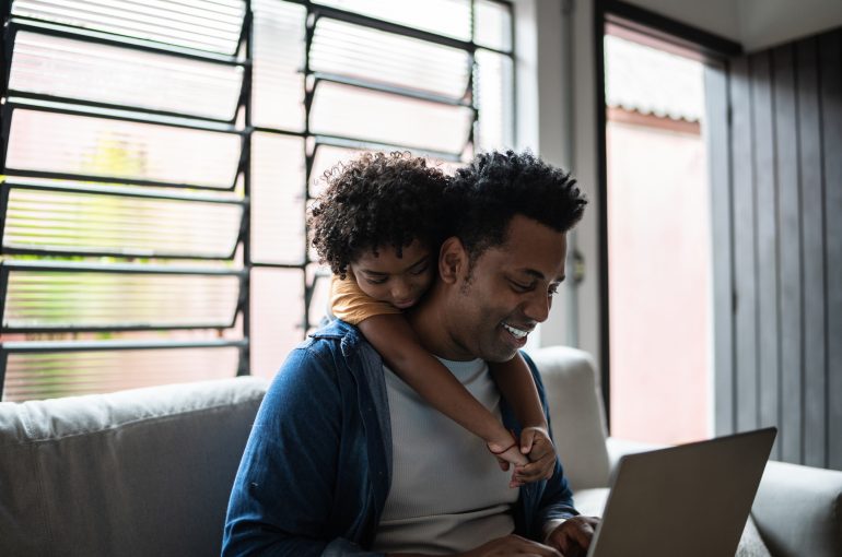 A young child hangs off of his father's back while they shop online